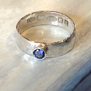 Silver hammered ring set with a beautiful 4mm round dark blue sapphire, hallmarked.